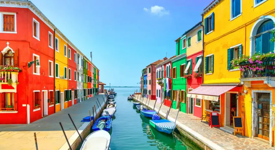 Coloratissime case affacciate su un canale, con barche ormeggiate. Un'immagine che invita a scoprire le splendide venezia isole da visitare.