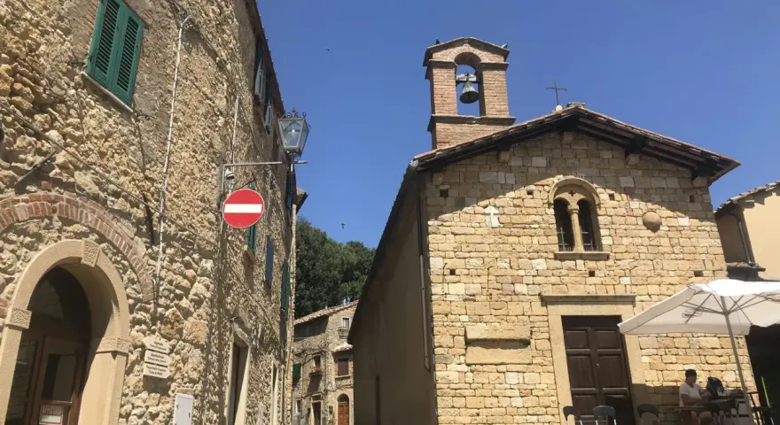 Un vicolo a Casale Marittimo, Pisa, con edifici in pietra, una chiesa con campanile e un tavolino all'aperto.
