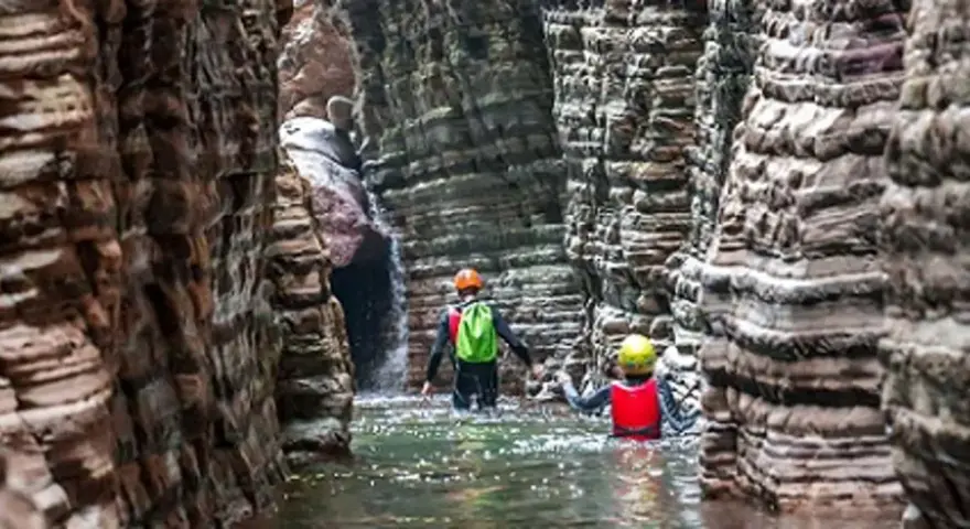 Esploratori in un canyon, tra rocce stratificate e acqua limpida, attraversano i **stretti di giaredo**.