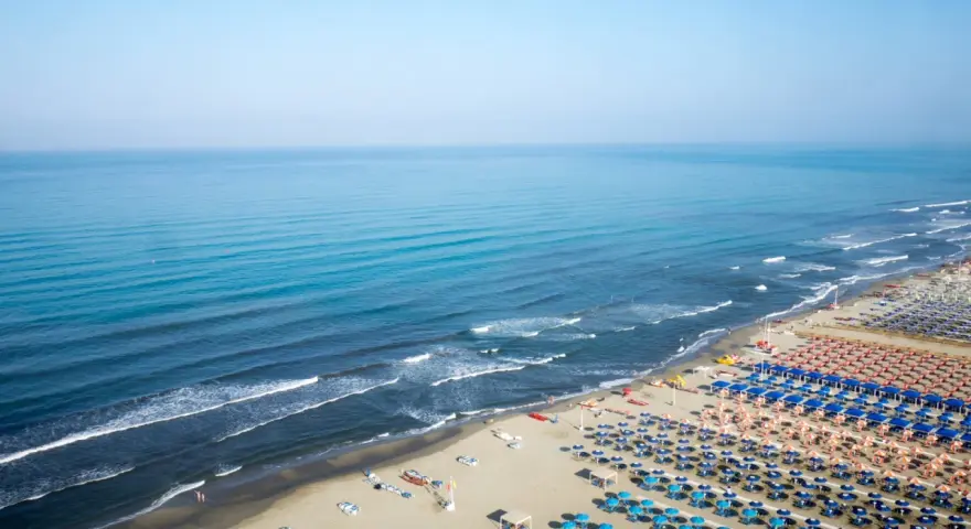 Ampia spiaggia libera al Lido di Camaiore, con file ordinate di ombrelloni e lettini che si estendono verso il mare azzurro.