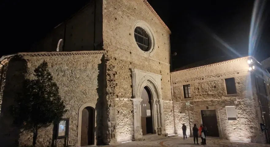 La chiesa di San Giovanni in Fiore illuminata di notte, con la sua facciata in pietra e il rosone circolare.
