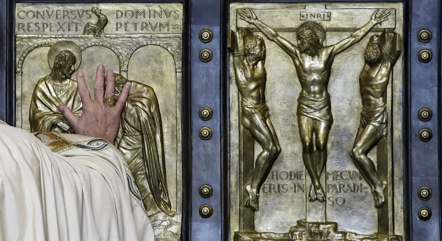 Mano che tocca la porta santa San Pietro, con scene della crocifissione e del rinnegamento di Pietro.