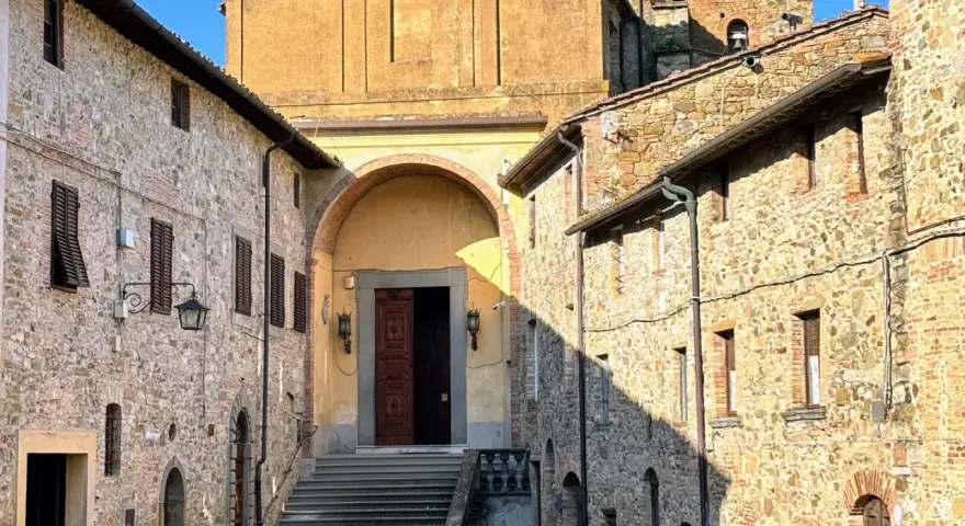 Chianni cosa vedere: un vicolo con case in pietra, una chiesa con un grande portale in legno e una scalinata.
