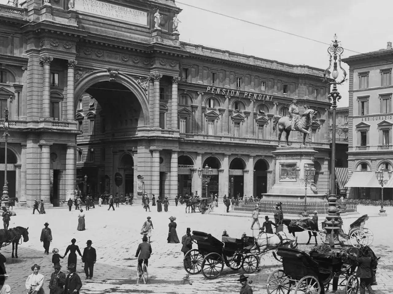 Piazza della Repubblica a Firenze, con la statua equestre, carrozze e gente passeggia.