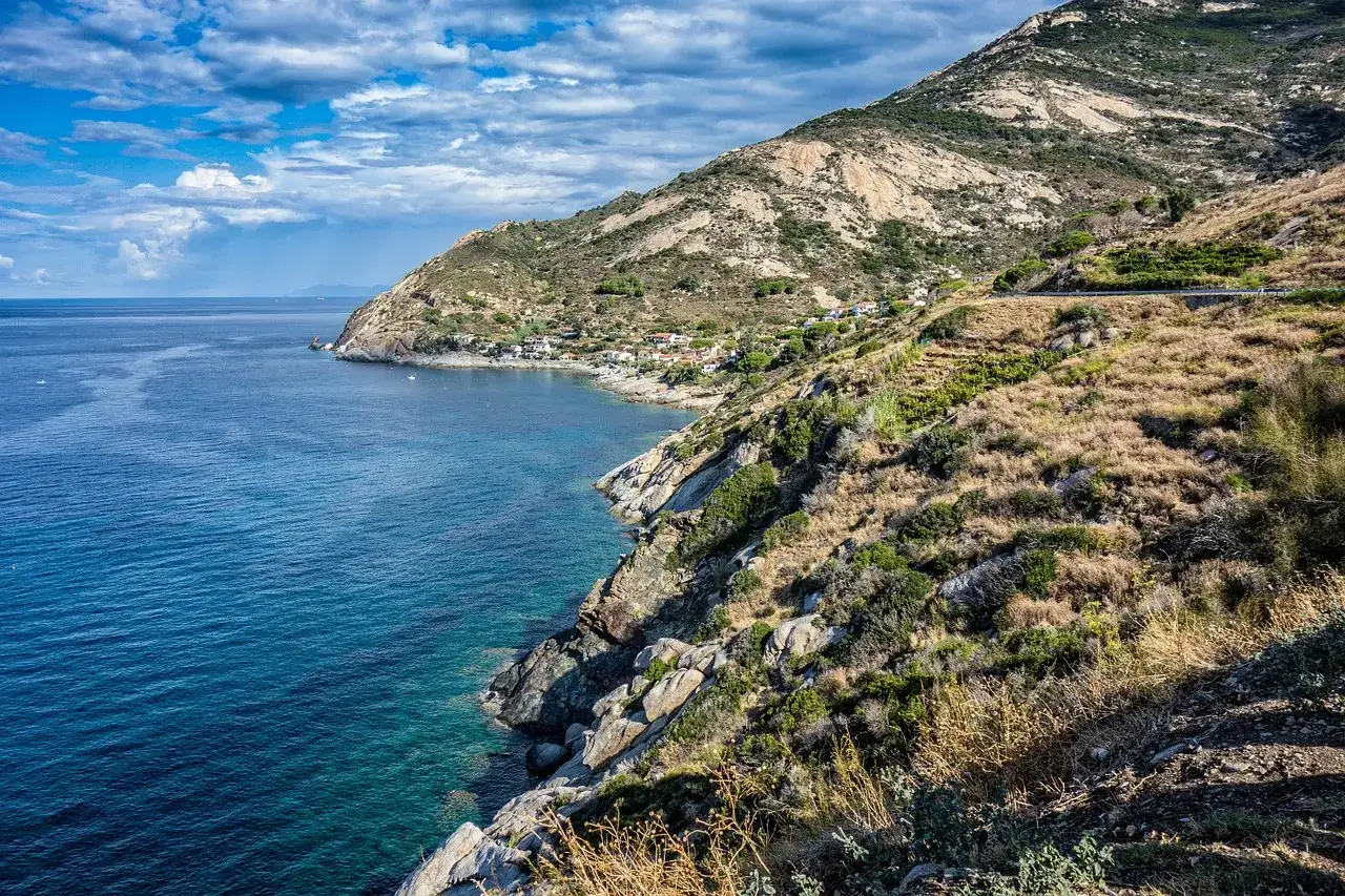 Costa rocciosa e mare blu all'Isola d'Elba. Un villaggio si affaccia sulla baia, ideale per scoprire cosa fare all'isola d'Elba.
