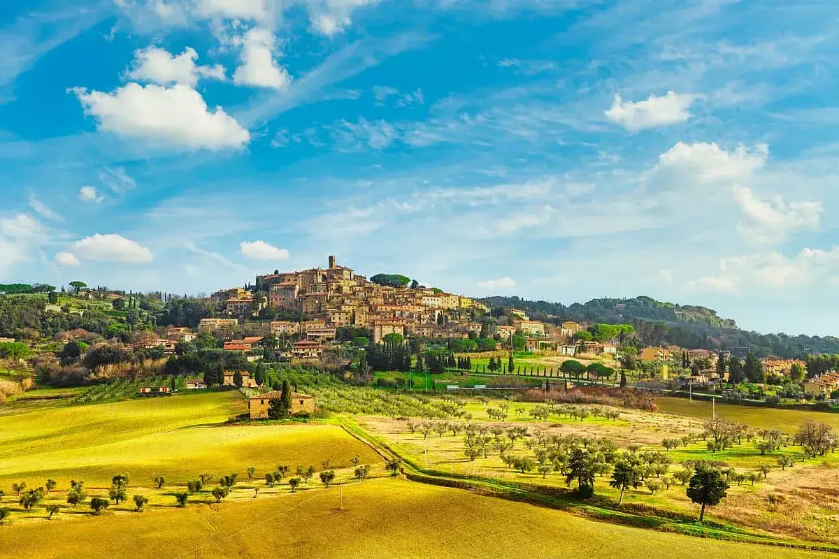 Panoramica di Casale Marittimo, borgo medievale in provincia di Pisa, con campi dorati e uliveti sotto un cielo azzurro.