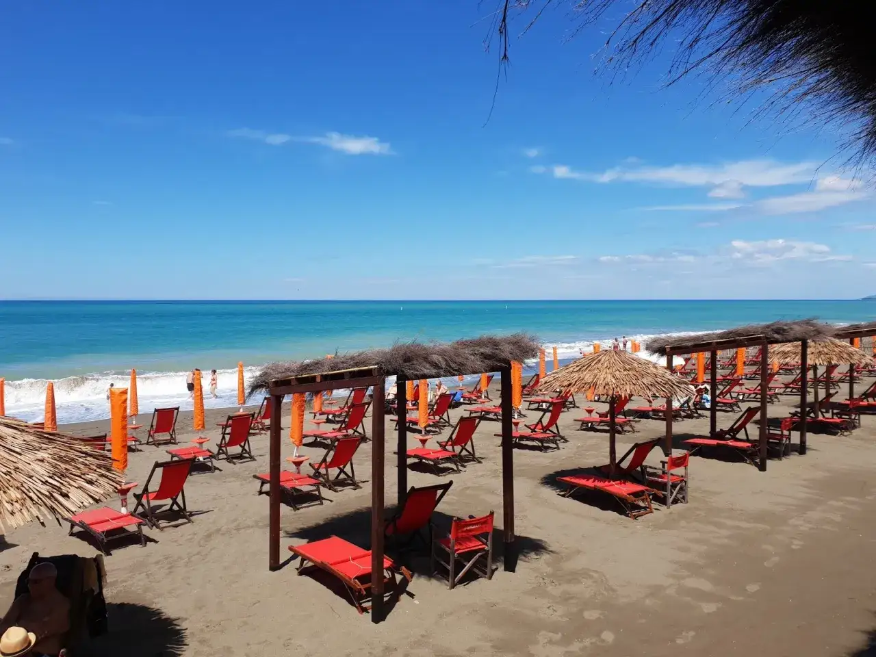 Spiaggia attrezzata a Marina di Bibbona, con lettini rossi, ombrelloni di paglia e il mare azzurro all'orizzonte.