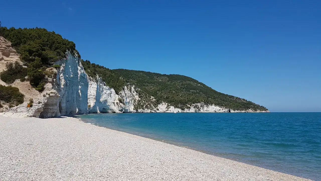 Scogliera bianca a picco sul mare turchese, con una spiaggia di ciottoli bianchi. Un angolo di paradiso, una spiaggia bianca Puglia da sogno.