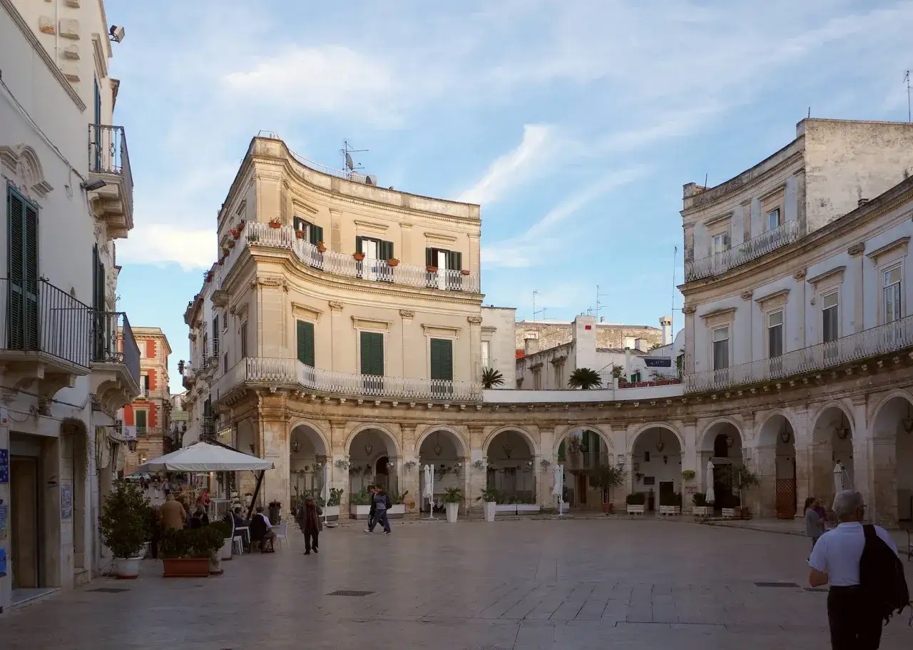 Piazza a Martina Franca con portici eleganti, palazzi barocchi e gente che passeggia.