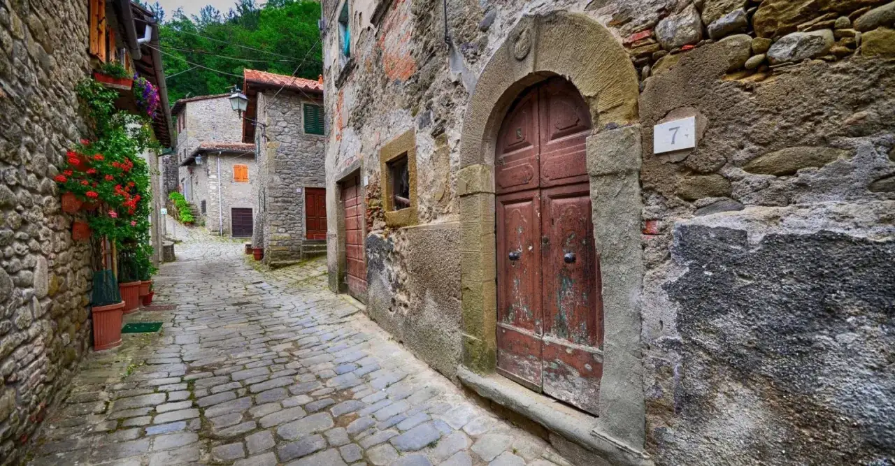 Antica strada in Casentino con case in pietra e fiori rossi.