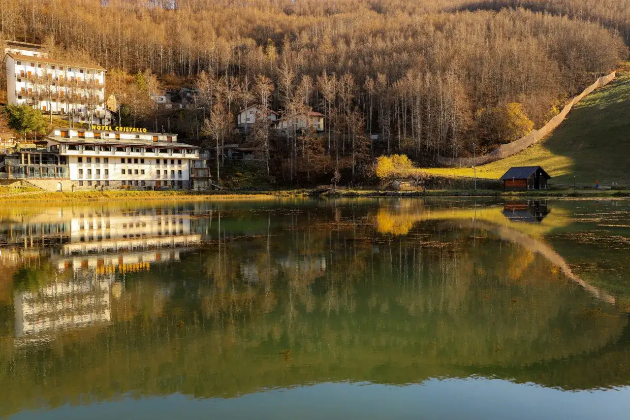 Hotel Cristallo sul Passo del Cerreto, riflesso in un lago tranquillo circondato da boschi autunnali.