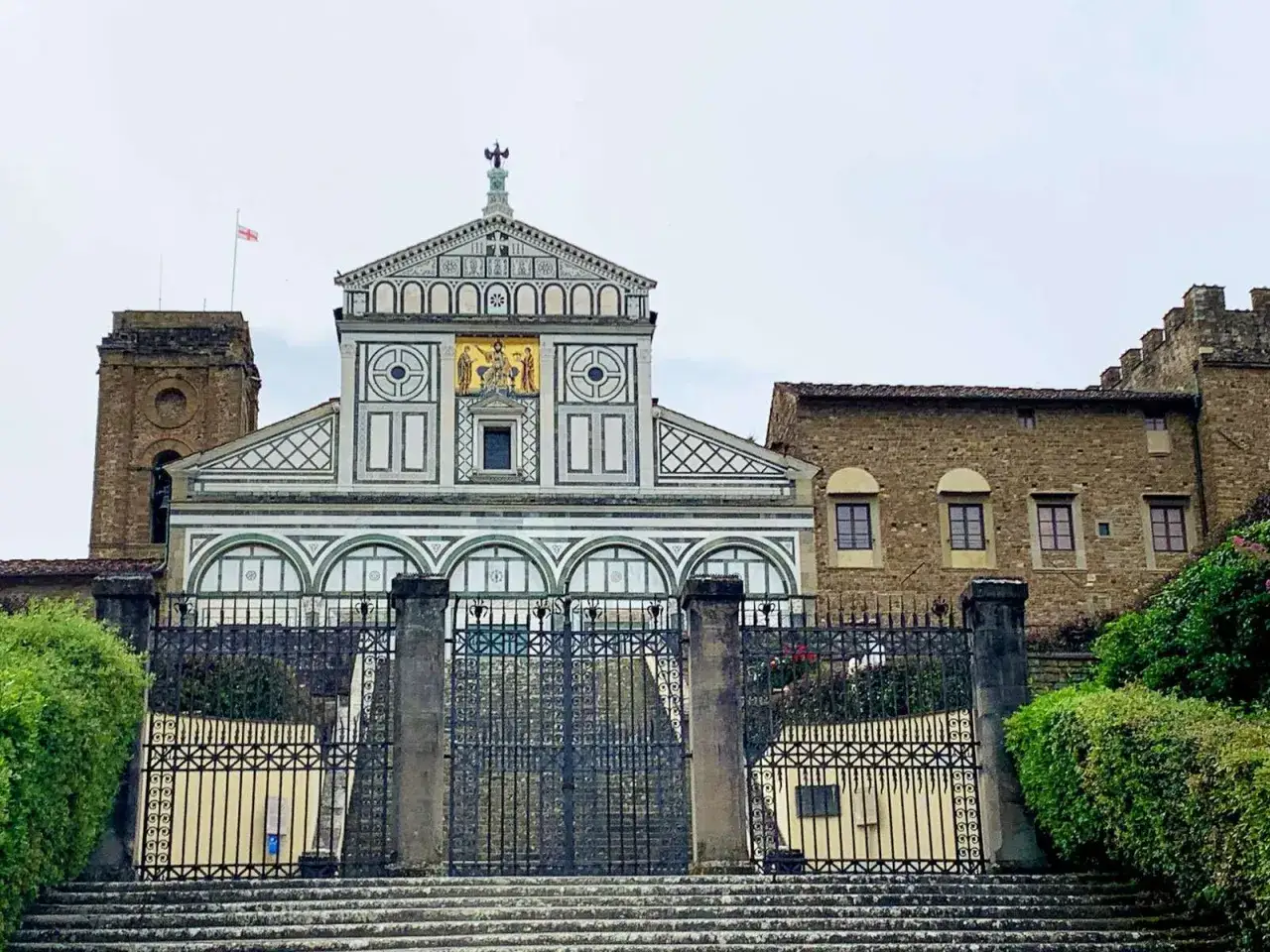 La facciata decorata di San Miniato al Monte, con il suo campanile e un cancello in ferro battuto, domina la vista.