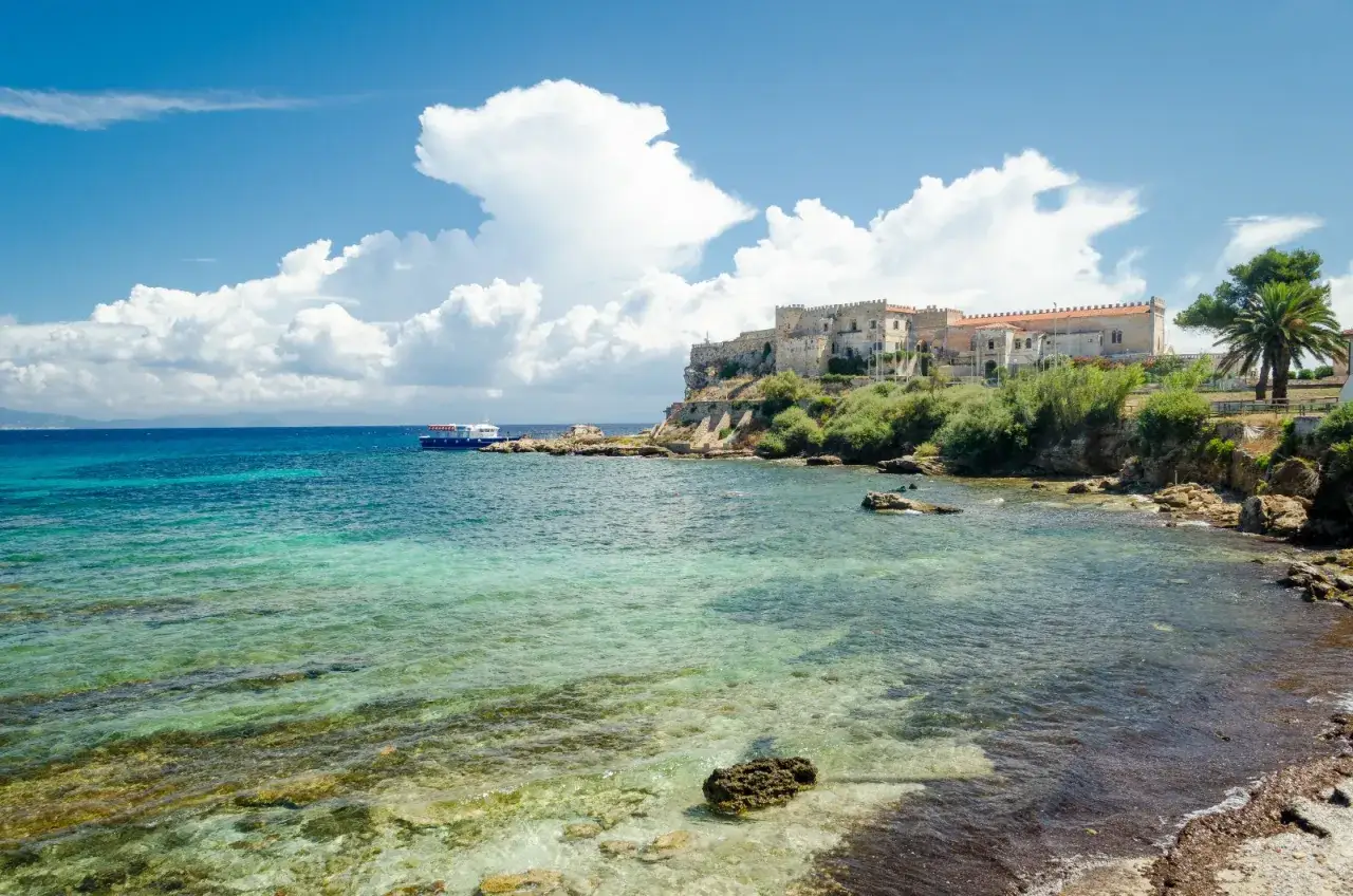 Un'isola vicina all'Elba con un castello imponente su una scogliera, acque cristalline e un battello all'orizzonte.
