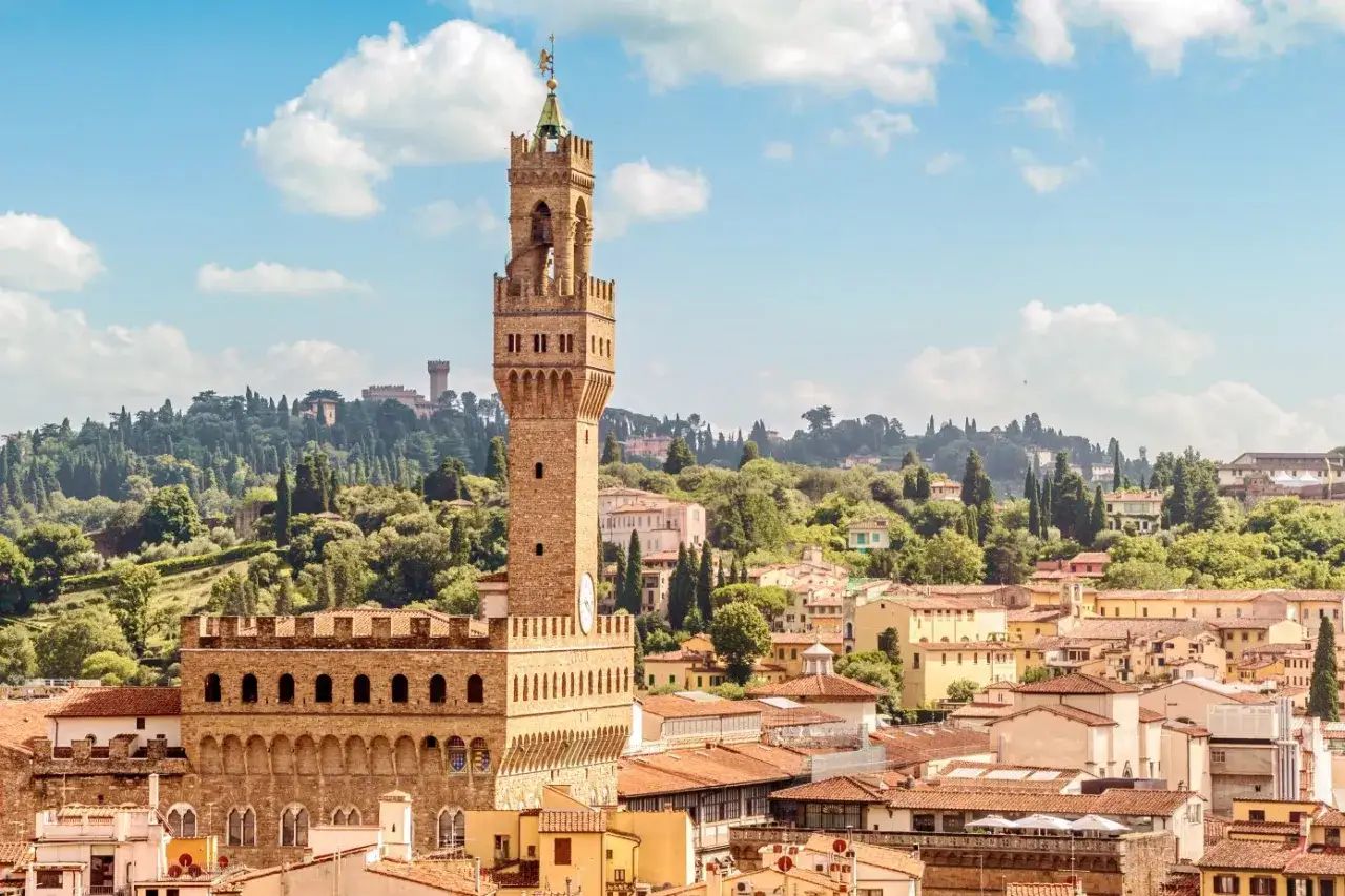 Il Palazzo Vecchio domina il panorama fiorentino, con la sua torre imponente che si staglia contro il cielo azzurro e le colline verdi.