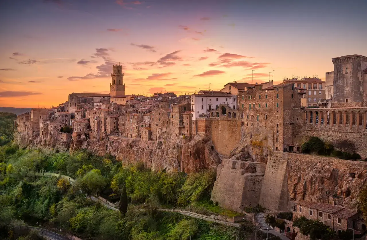 Il pittoresco centro storico di Pitigliano si staglia su una rupe tufacea al tramonto, con case antiche e una torre imponente.