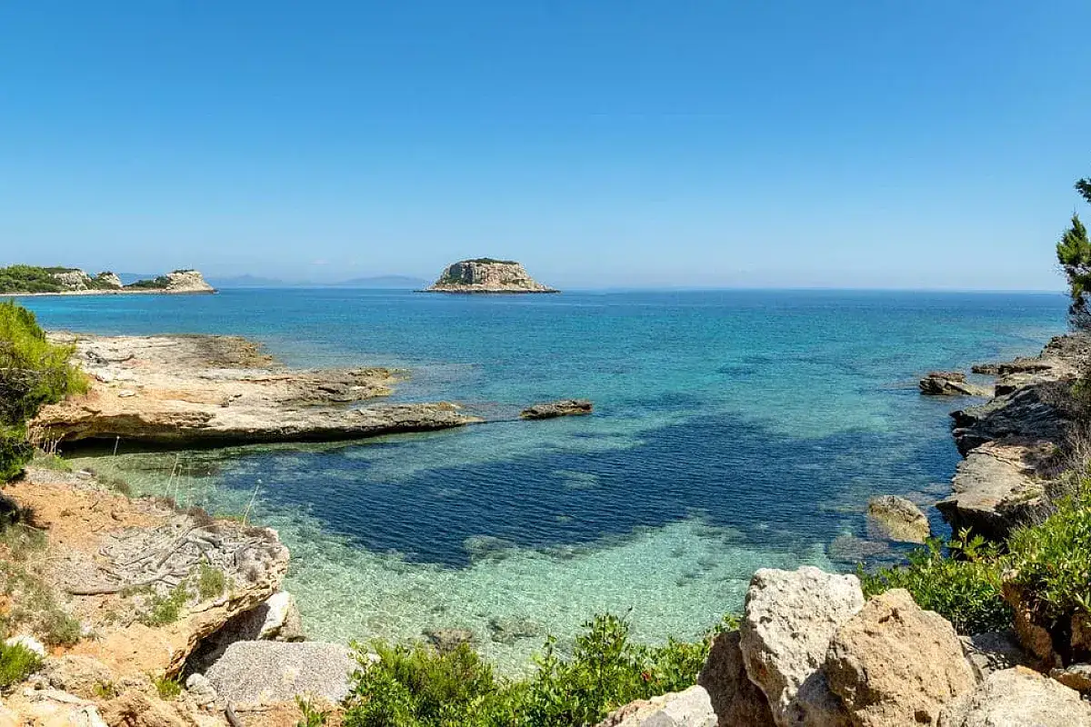 Scogliera rocciosa e mare cristallino con un isolotto in lontananza, un angolo di paradiso sull'isola di Pianosa.