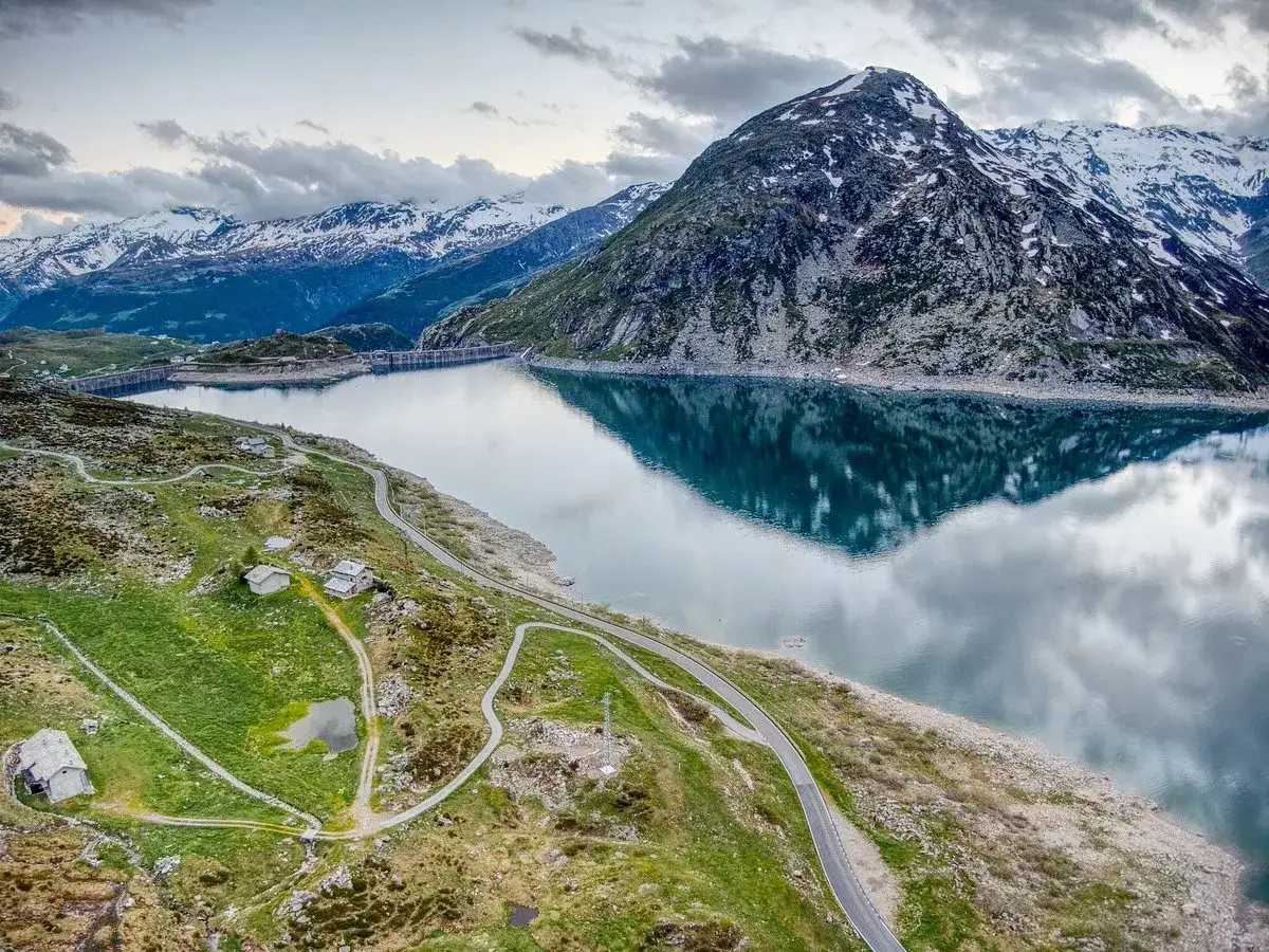 Lago alpino con diga e montagne innevate, vicino al passo dello Spluga. Strade tortuose e case isolate.