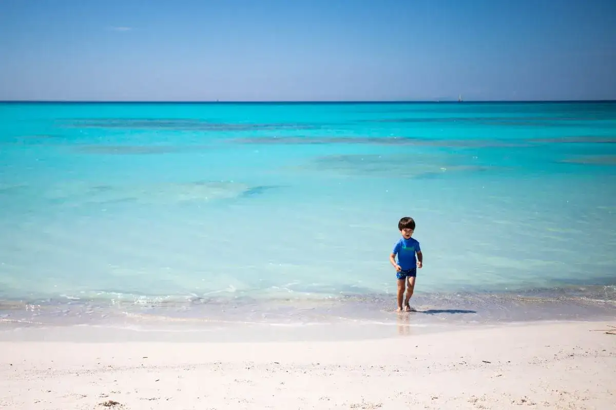 Bambino corre felice sulle spiagge bianche di Rosignano, con il mare turchese che lambisce la riva.