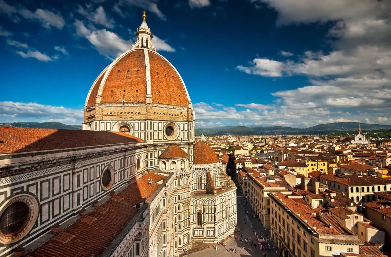 La cupola del Duomo domina la piazza del Duomo a Firenze, con la città che si estende all'orizzonte sotto un cielo azzurro e nuvoloso.