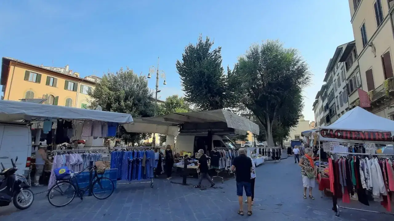 Mercato all'aperto in piazza Santo Spirito, Firenze. Bancarelle di abbigliamento e accessori sotto il sole, con edifici storici sullo sfondo.