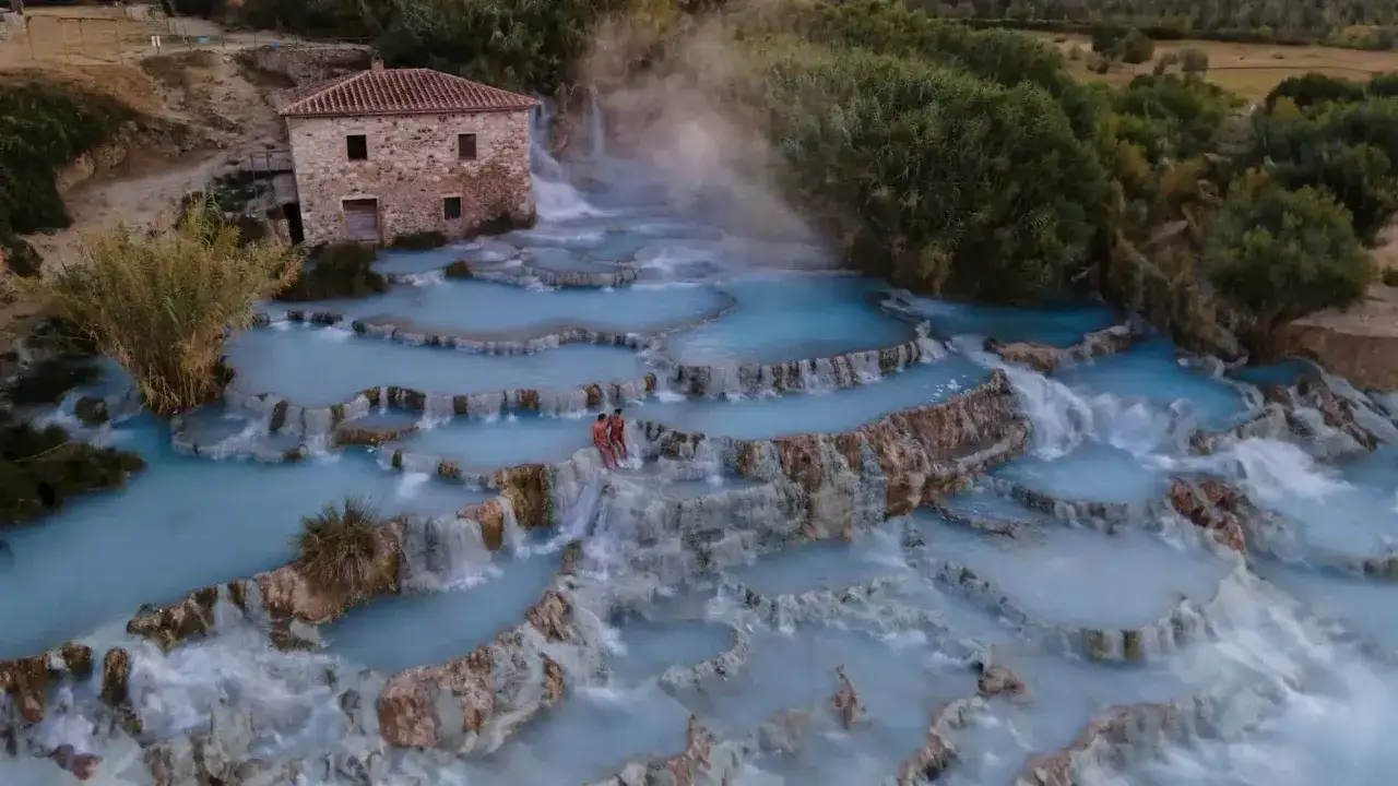Cascate termali azzurre vicino al molinetto della Croda, con due persone che si godono il panorama.
