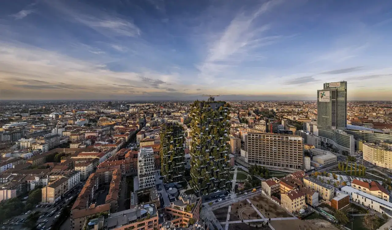 Il Bosco Verticale di Milano, un'icona di architettura sostenibile, si staglia tra i palazzi della citt&agrave; sotto un cielo limpido.