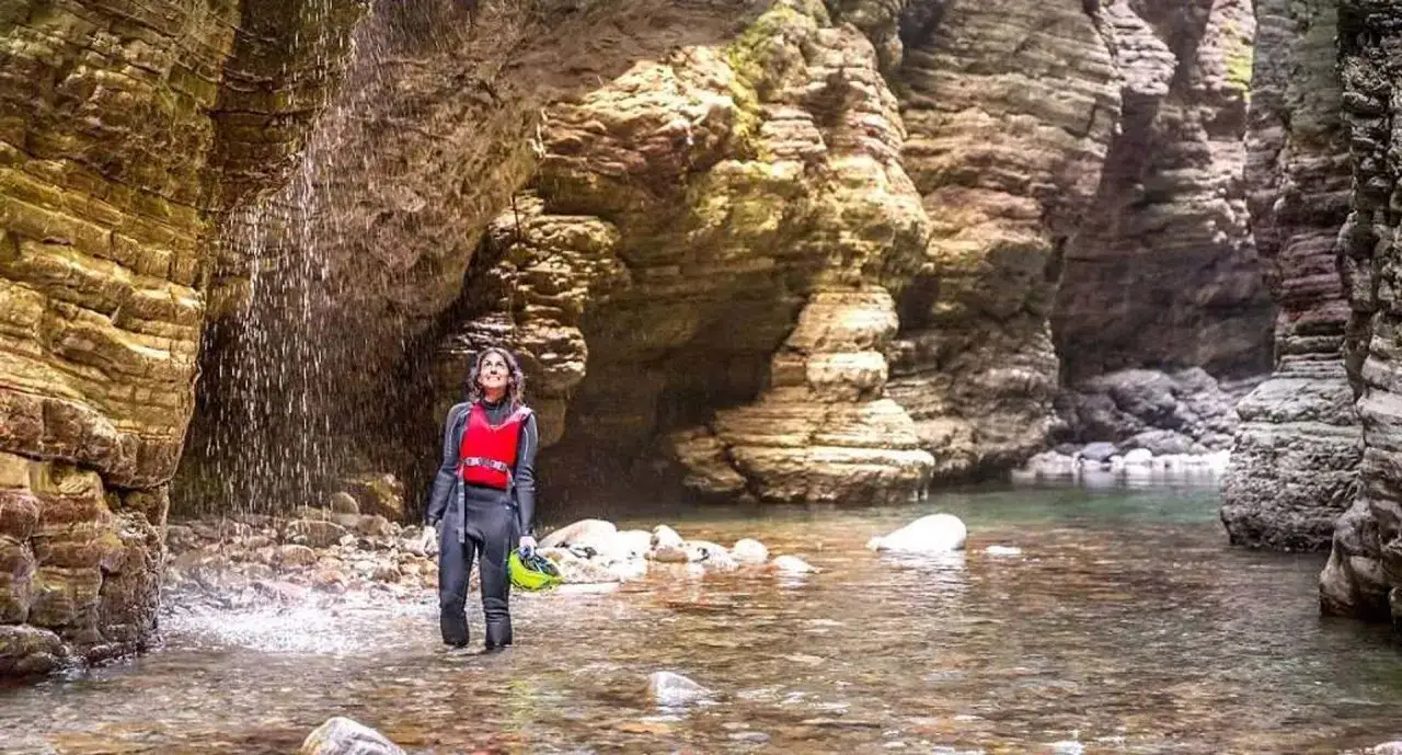 Donna in muta e giubbotto salvagente ammira una cascata negli stretti di giaredo, circondata da imponenti pareti rocciose.