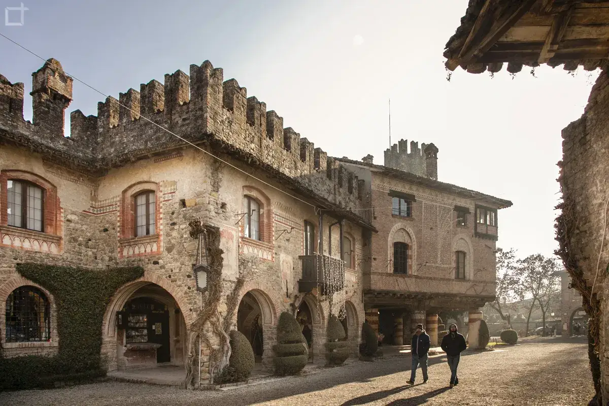 Due uomini passeggiano nel borgo di Grazzano Visconti, tra antichi palazzi in pietra e mattoni con merlature e archi.