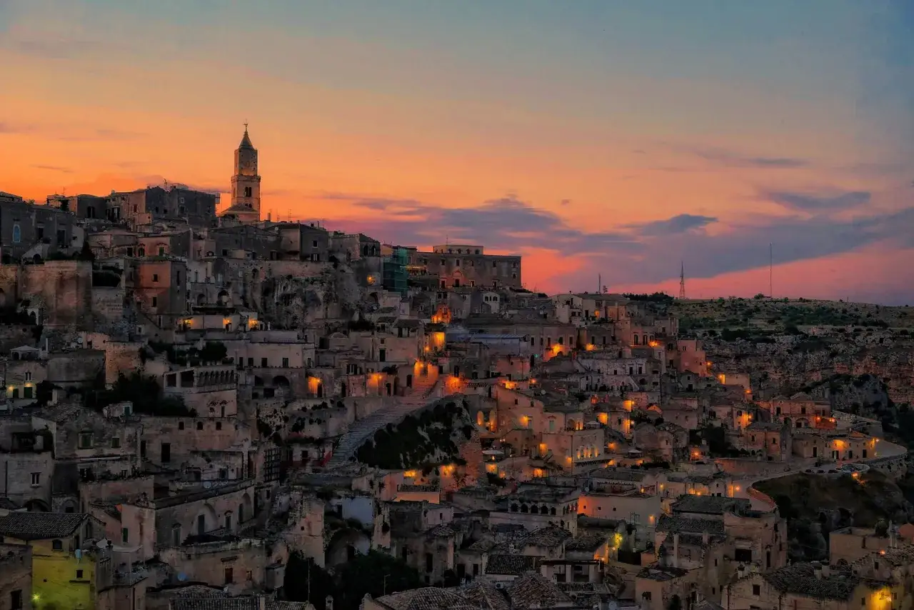 I Sassi di Matera illuminati al tramonto, un panorama mozzafiato di case scavate nella roccia sotto un cielo arancione.