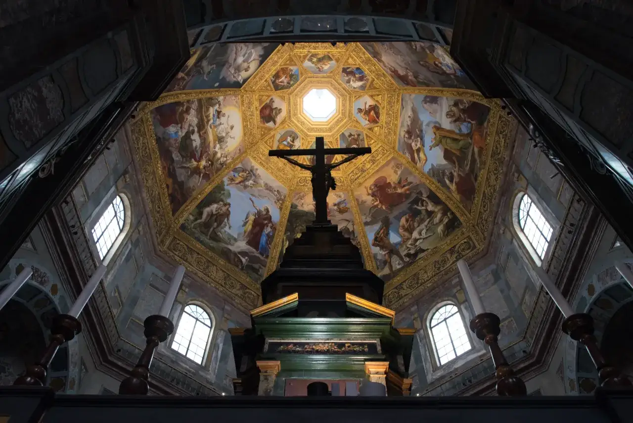 Interno delle Cappelle Medicee a Firenze: crocifisso imponente sotto una cupola affrescata con scene bibliche e candelabri.