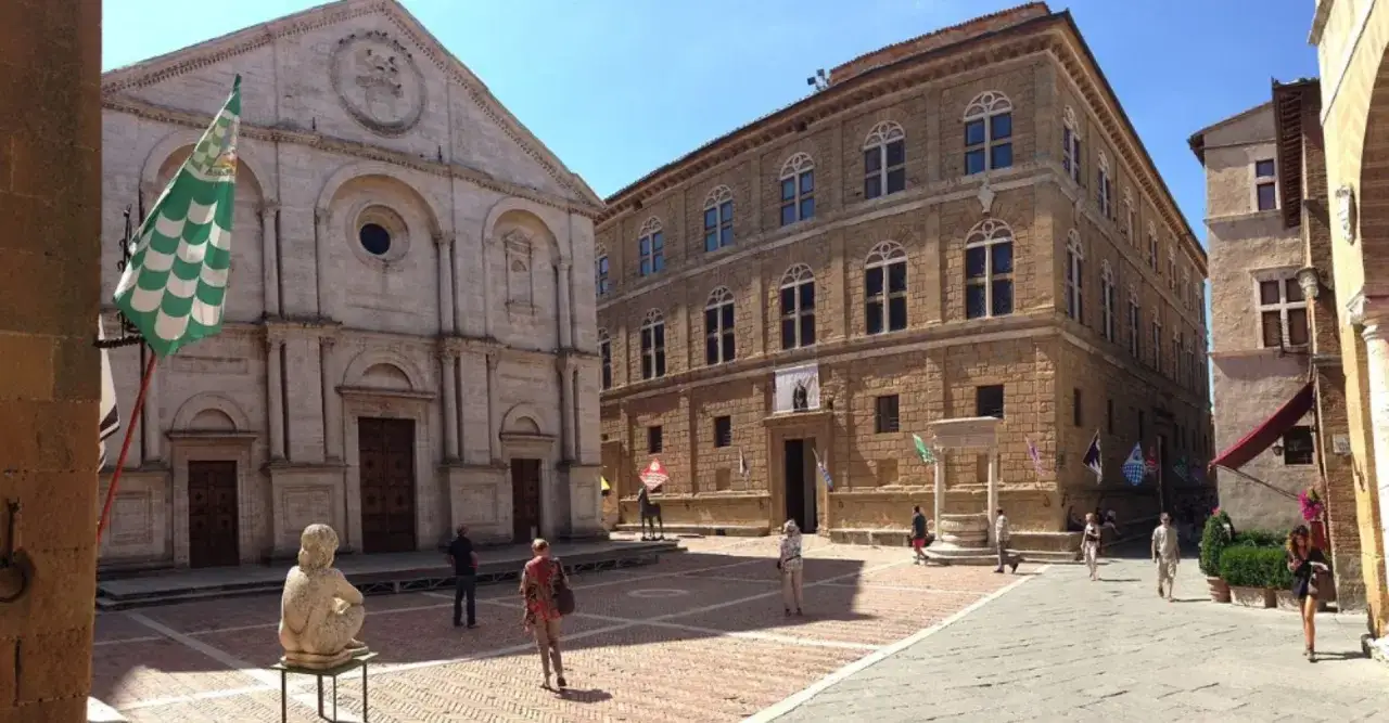 Piazza Pio II a Pienza, con la cattedrale e il Palazzo Piccolomini. Una giornata di sole con turisti che passeggiano.