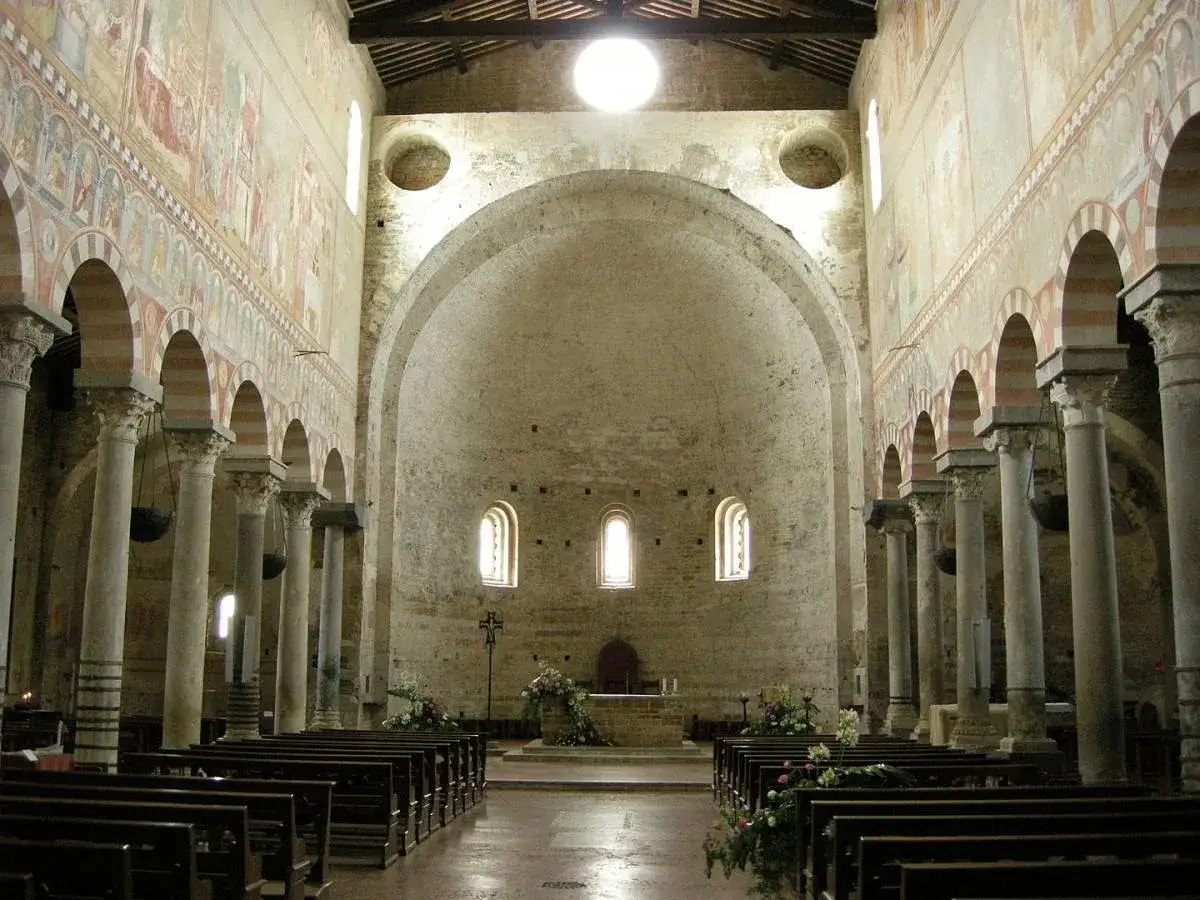 Interno della Basilica di San Piero a Grado, con affreschi antichi, colonne imponenti e panche in legno.