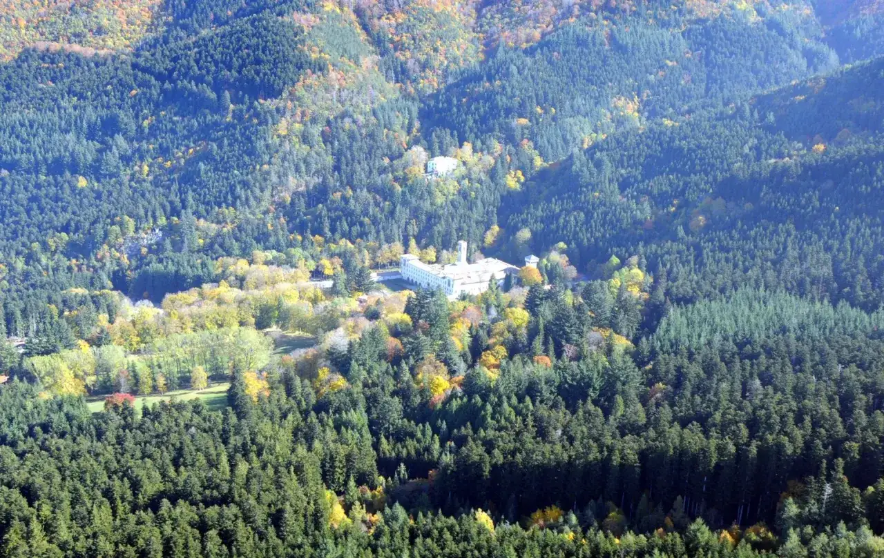 Vista aerea della foresta di Vallombrosa con un grande edificio bianco in mezzo agli alberi autunnali dai colori vivaci.