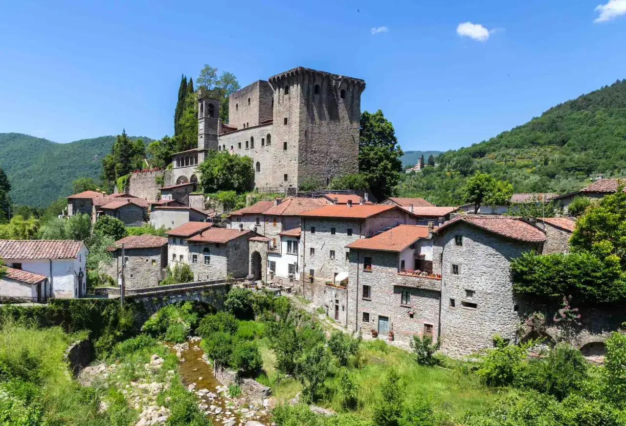 Fivizzano cosa vedere: un borgo medievale con castello, case in pietra e un ponte su un ruscello, immerso nel verde delle colline.