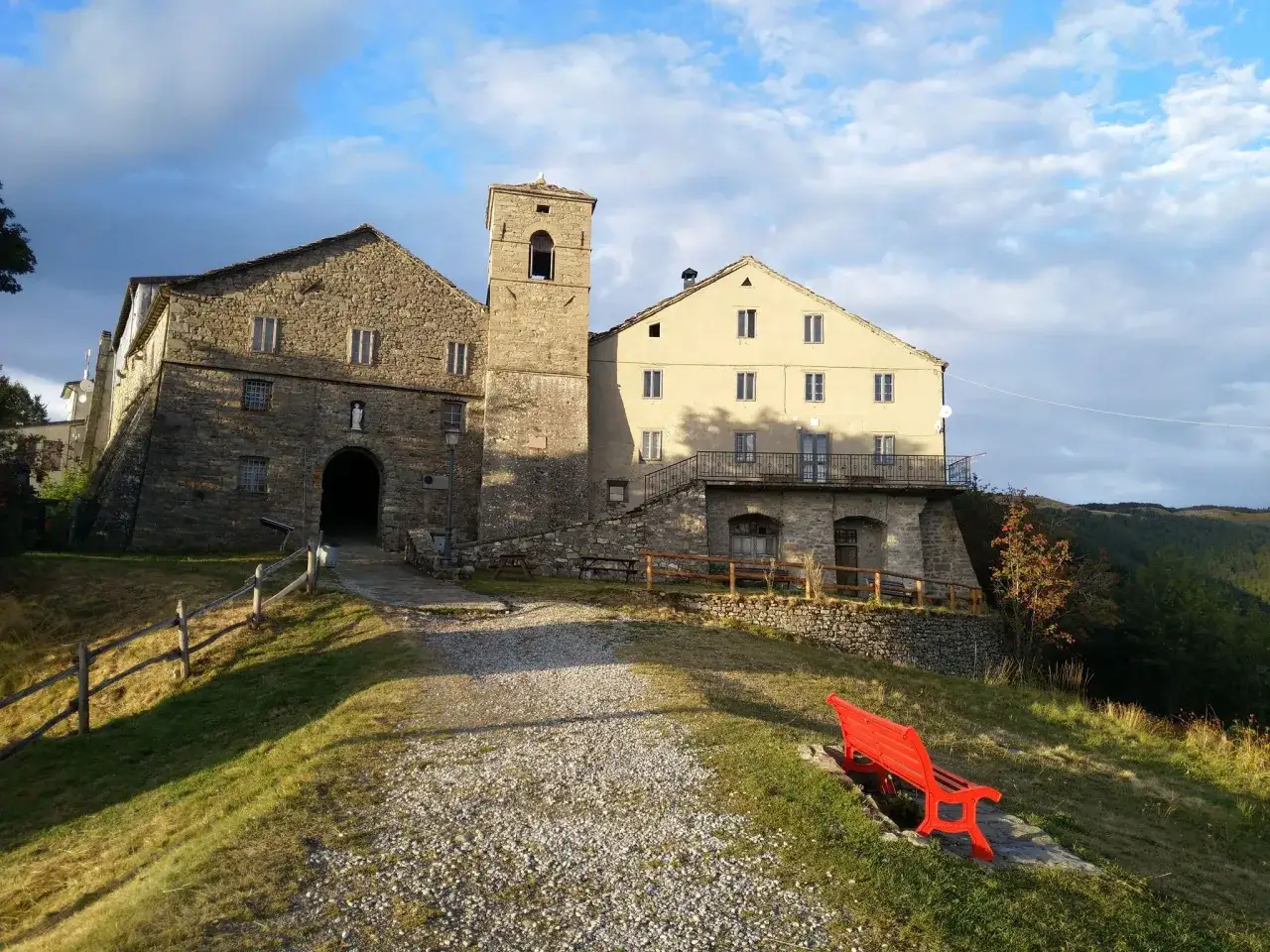 Antico complesso di San Pellegrino in Alpe con campanile e panchina rossa, sotto un cielo nuvoloso.