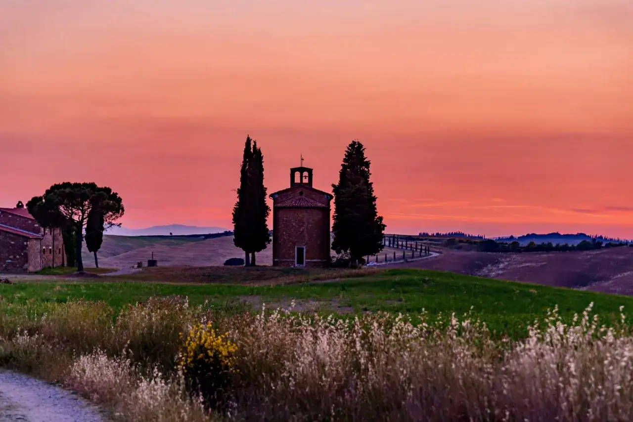 Cappella nel Val d'Orcia al tramonto, con colline ondulate e cipressi.