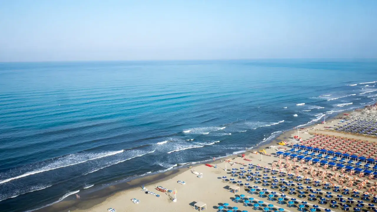 Ampia spiaggia libera al Lido di Camaiore, con file ordinate di ombrelloni e lettini che si estendono verso il mare azzurro.