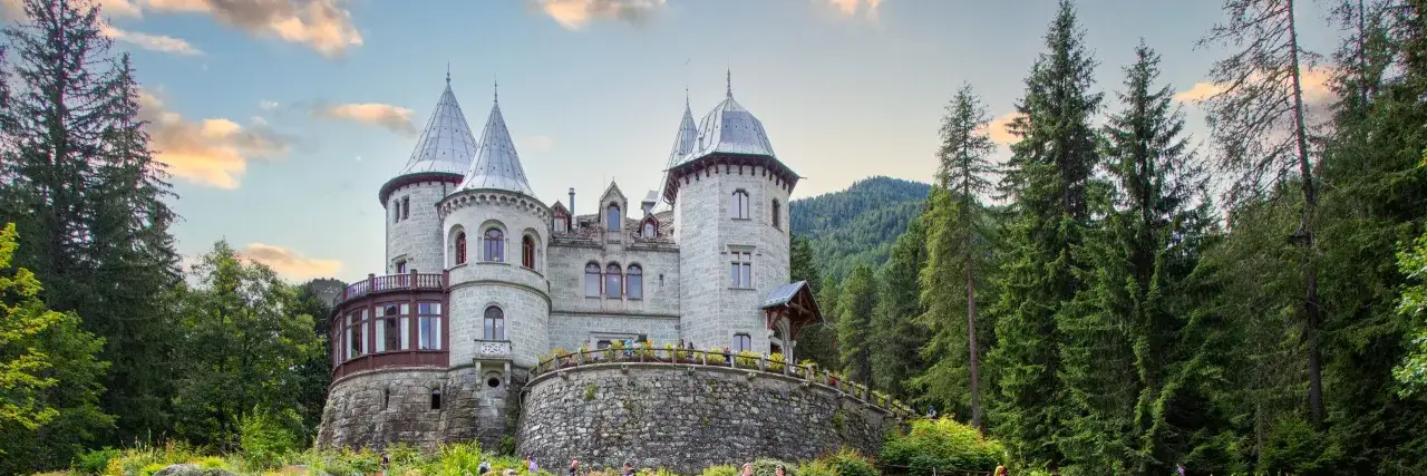 Un fiabesco castello in pietra, con torri coniche e un balcone curvo, immerso nel verde dei boschi della Val d'Aosta.