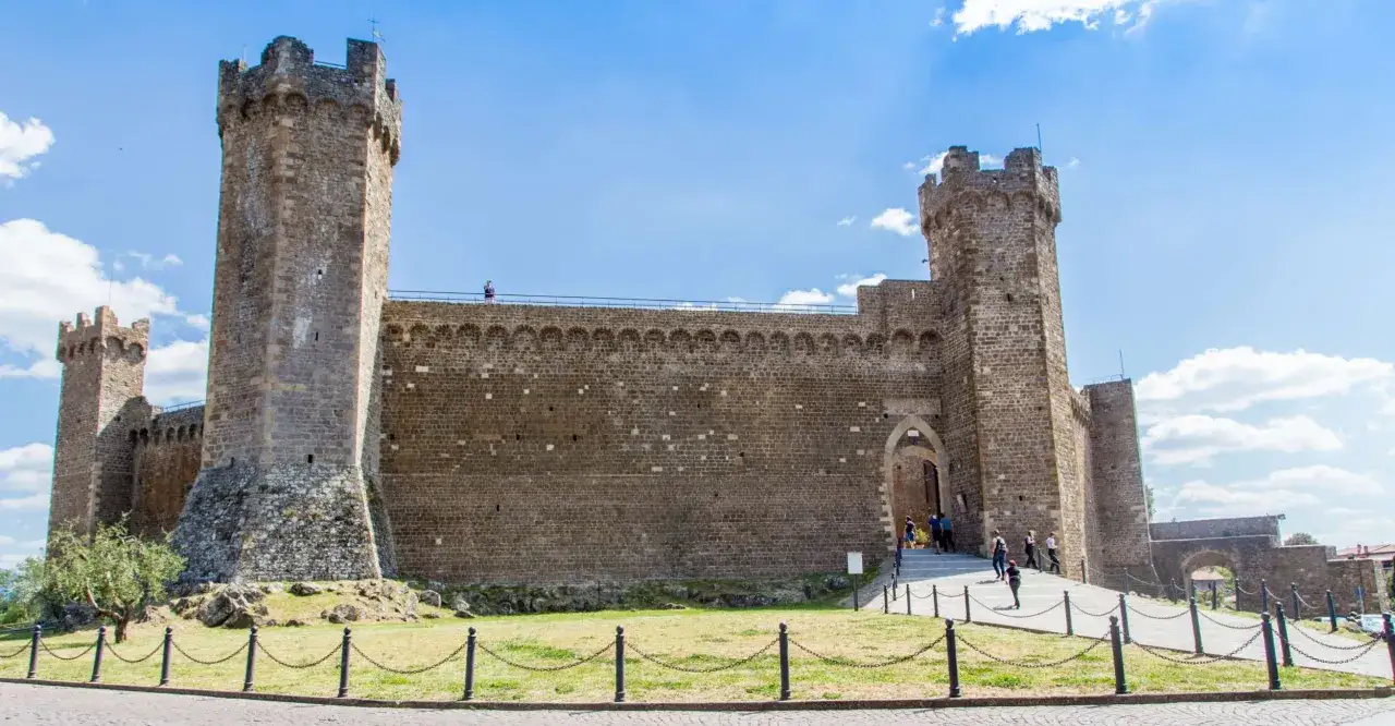 La fortezza di Montalcino, con le sue imponenti torri e mura in pietra, domina il paesaggio toscano sotto un cielo azzurro.