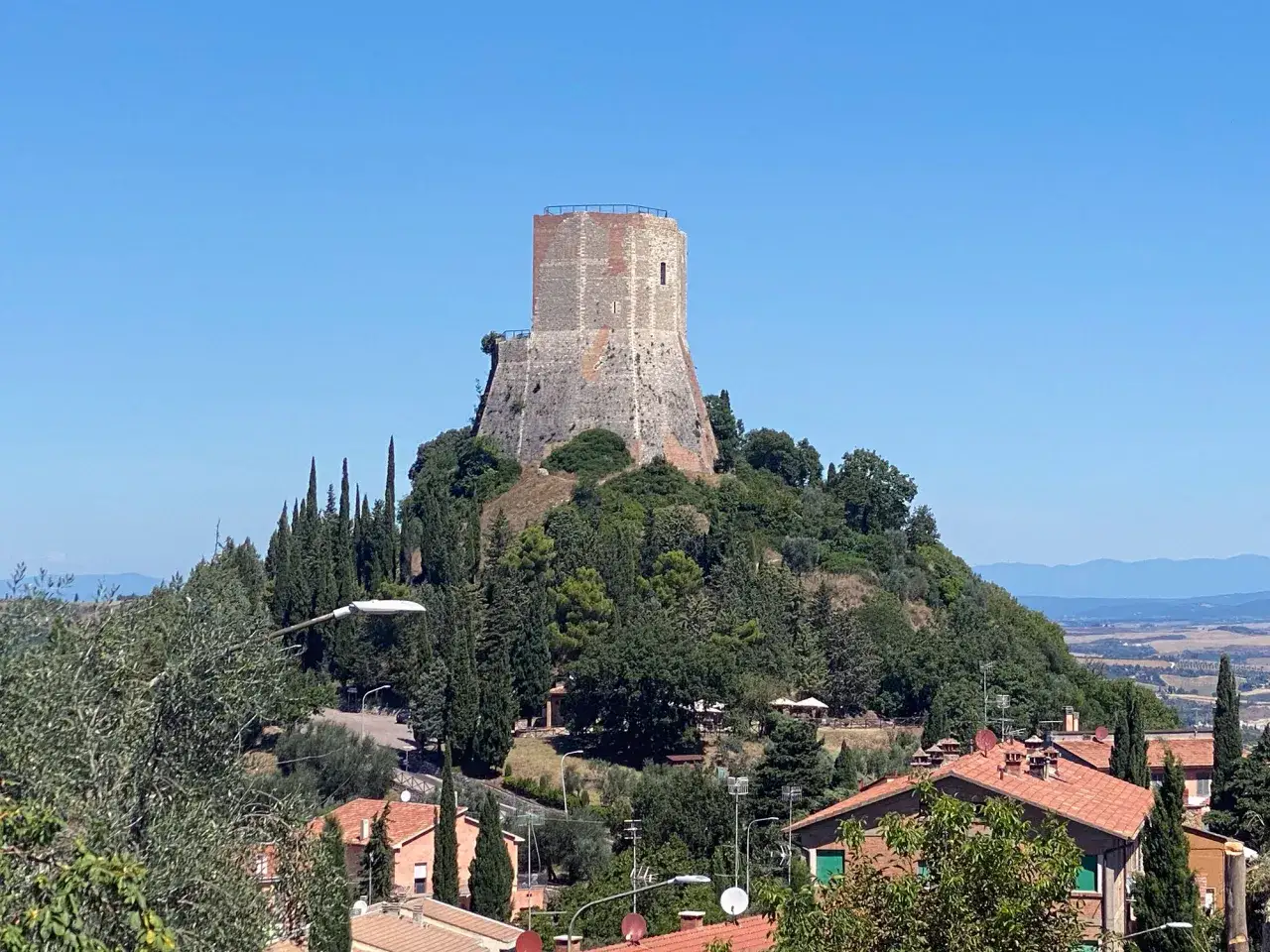 La rocca di Tentennano domina il paesaggio collinare toscano, circondata da cipressi e case con tetti rossi.