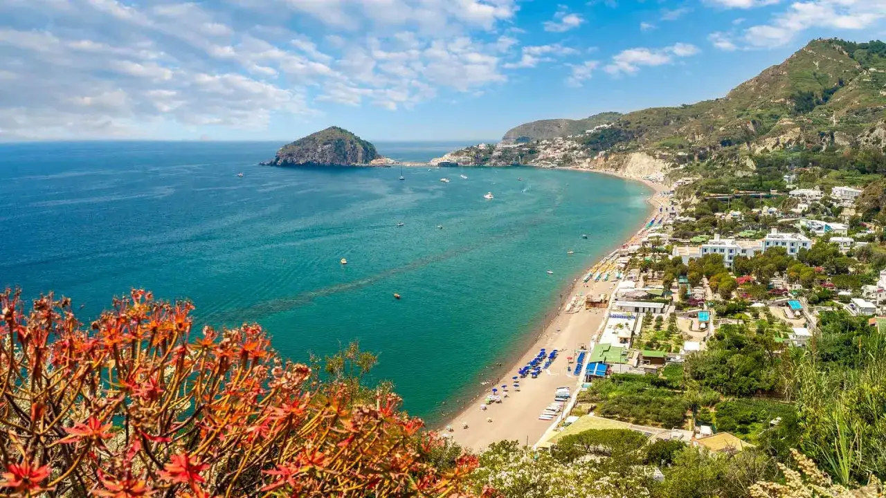 Vista panoramica della spiaggia dei Maronti con acque turchesi, ombrelloni colorati e case arroccate sulla collina.