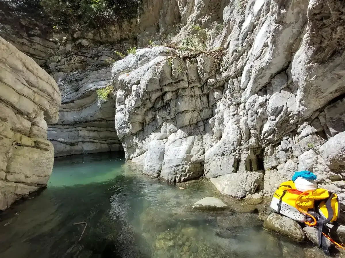 Acqua cristallina nel canyon dell'Orrido di Botri, tra pareti rocciose imponenti. Zaino giallo pronto per l'avventura.