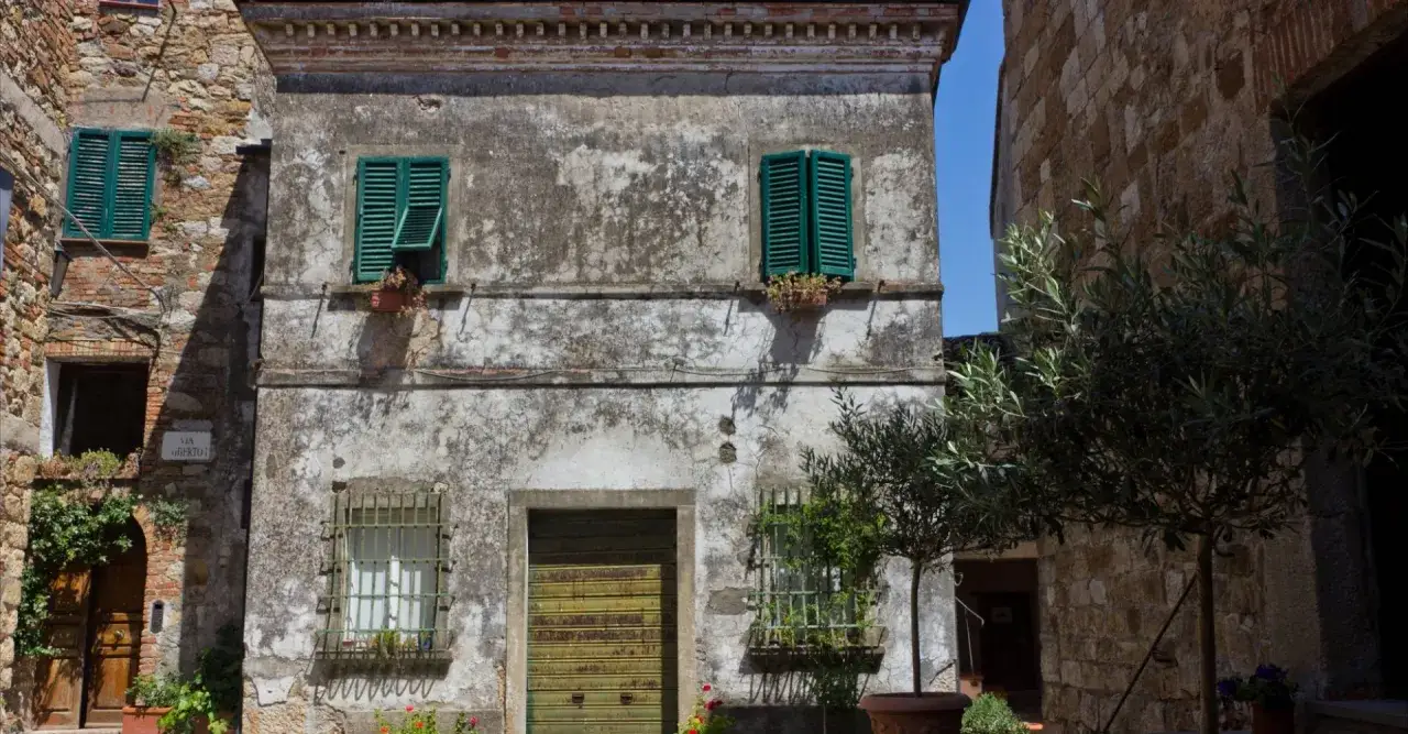 Un vicolo pittoresco a Monteverdi Marittimo cosa vedere: un'antica facciata con persiane verdi, un ulivo e scorci suggestivi.