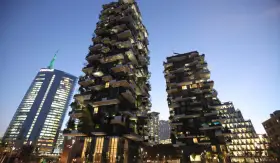 Il Bosco Verticale di Milano, con i suoi grattacieli ricoperti di alberi e piante, si staglia contro il cielo serale.