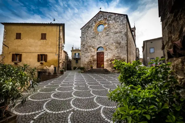 Piazza di Bibbona, cosa vedere: chiesa in pietra con rosone, case gialle e pavimentazione a ventaglio.