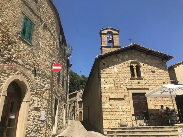 Un vicolo a Casale Marittimo, Pisa, con edifici in pietra, una chiesa con campanile e un tavolino all'aperto.