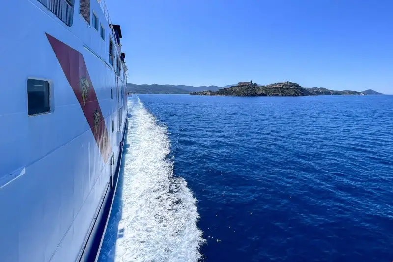 Traghetto in navigazione verso l'isola d'Elba, con la costa all'orizzonte sotto un cielo azzurro.