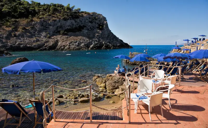 Le argentario spiagge più belle, con ombrelloni blu e lettini su una terrazza in legno, affacciate sul mare cristallino.