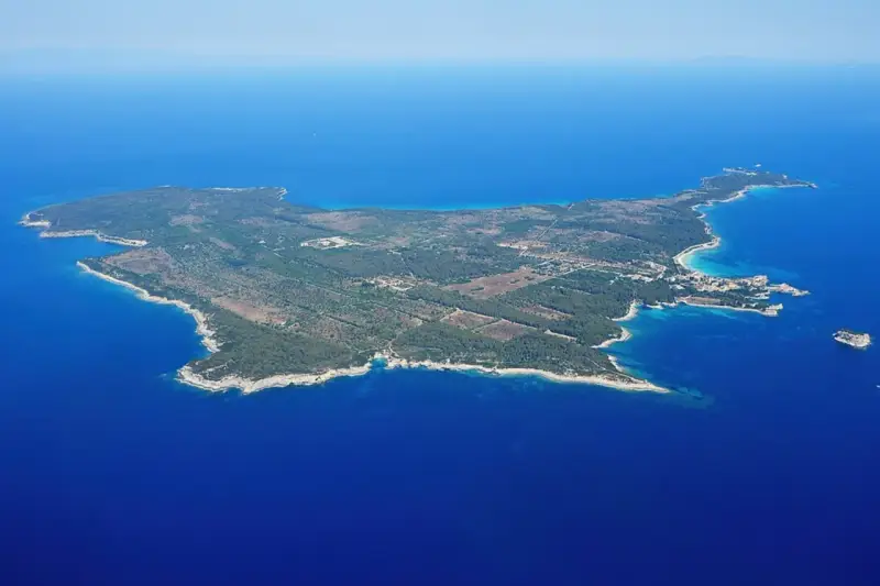 Vista aerea di un'isola verdeggiante, un'isola vicino all'Elba, con acque blu intenso e una piccola isola rocciosa in lontananza.